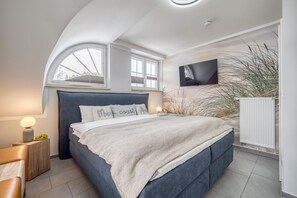Een slaapkamer met een bed, bedlampen, een televisie en een raam.