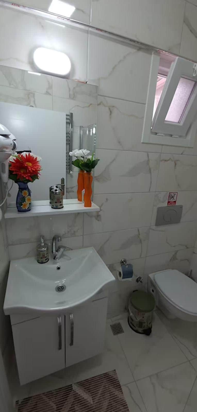 Un baño con lavamanos blanco, espejo e inodoro. Hay dos floreros sobre el lavamanos.