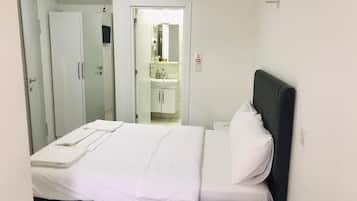 A hotel room with a bed, a bedside table, a wardrobe, and a bathroom visible through an open door.