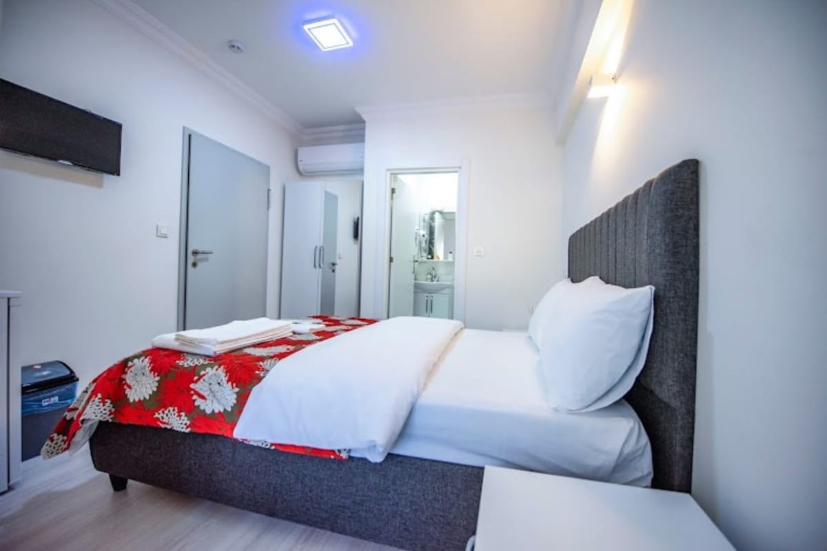 Una habitación de hotel moderna con una cama, un televisor de pantalla plana montado en la pared y una puerta que da a un baño.