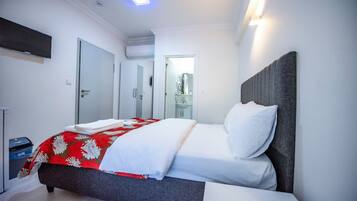 Ein modernes Hotelzimmer mit einem Bett, einem an der Wand befestigten Flachbildfernseher und einer Tür zu einem Badezimmer.