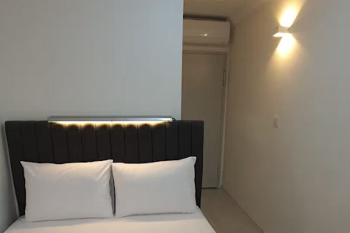Ein ordentlich bezogenes Bett mit weißen Leinen und Kissen, ein Kopfteil und eine Wandleuchte.