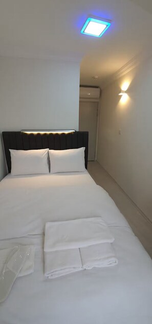 Ein ordentlich bezogenes Bett mit weißen Leinen und Kissen, ein Kopfteil und eine Wandleuchte.