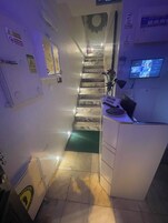 Un pasillo estrecho con una escalera que lleva a una zona de descanso, una recepción y un televisor montado.