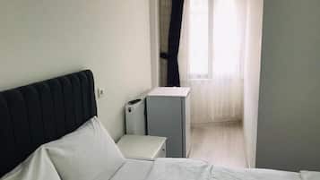 A hotel room with a bed, a bedside table, a small cabinet, and a window with sheer curtains.