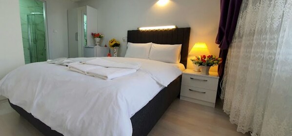 A neatly made bed with white linens, a bedside lamp, and a small table with a vase of flowers.