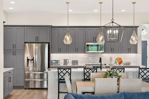 A modern kitchen with grey cabinets, stainless steel appliances, and pendant lighting. - Fairway Vista - 3/3 w/ 4-Seat Golf Cart in The Villages - Moultrie Creek (Moultrie Creek, The Villages)