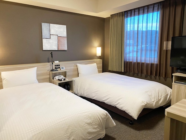 A hotel room with two beds, a flat-screen TV, a bedside table, a lamp, and a window with curtains. - Hotel Route-inn Yamagata South - in Front of University Hospital (Yamagata)