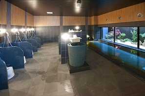 A modern bathroom with multiple urinals, a large stone basin, and a view of an indoor pool with aquatic plants. - Hotel Route-inn Yamagata South - in Front of University Hospital (Yamagata)