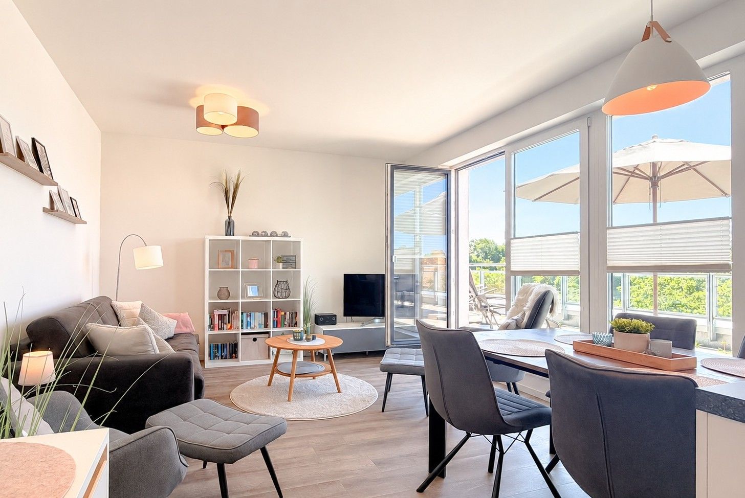 Un salon moderne comprenant un canapé, une table basse et des fauteuils, une bibliothèque, un téléviseur à écran plat et de grandes fenêtres donnant sur l’extérieur.