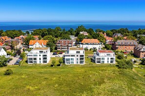 A coastal residential area with modern and traditional buildings, a clear view of the sea, and a bridge in the distance. - White Villas Penthouse 11 (Ostseebad Boltenhagen)