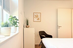 A bedroom with a bed, a chair, a desk, a potted plant, and a framed picture on the wall. - White Villas Penthouse 11 (Ostseebad Boltenhagen)