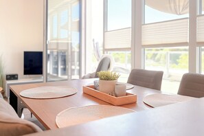 A modern dining area with a wooden table, woven placemats, a tray with a plant, and a candle. - White Villas Penthouse 11 (Ostseebad Boltenhagen)