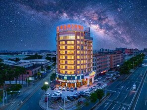 Un hotel de varios pisos con fachada curva, un estacionamiento y vistas de la Vía Láctea.
