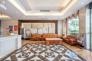 Un vestíbulo de hotel con un mostrador de recepción, sofás de cuero, piso estampado y un ventanal con vistas.