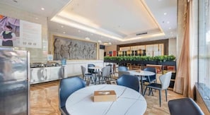Un comedor de hotel moderno con mesas redondas, asientos de bar y una cocina a la vista.