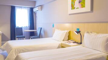 A hotel room with two beds, a desk, a chair, an air conditioning unit, and a painting on the wall.