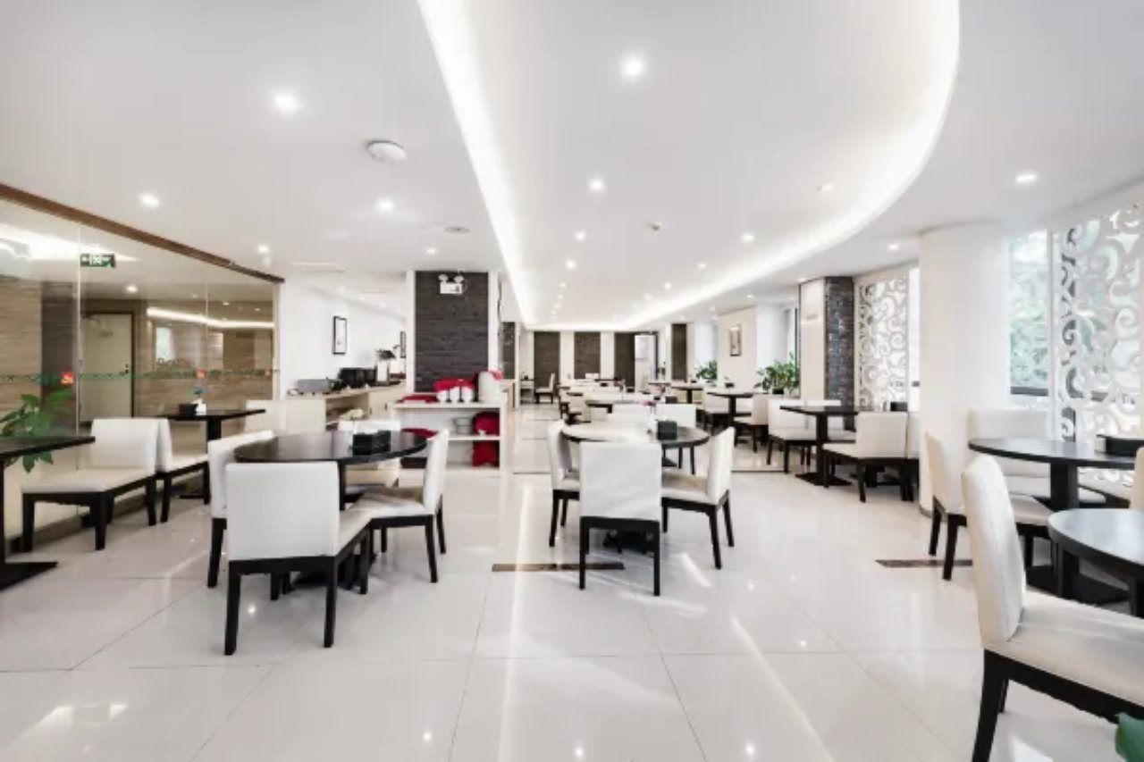 A modern hotel lobby with multiple dining areas, a reception desk, and a curved ceiling design.