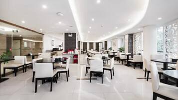 A modern hotel lobby with multiple dining areas, a reception desk, and a curved ceiling design.