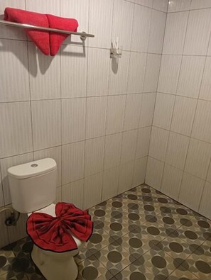 A bathroom with a toilet, a red towel on the seat, and patterned floor tiles. - Sunnyday inn Merauke (Merauke)