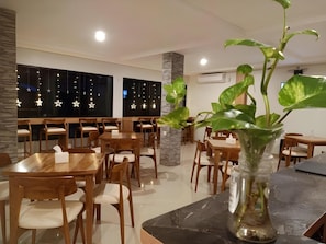 A restaurant interior with wooden tables and chairs, a central pillar, and hanging star-shaped lights.