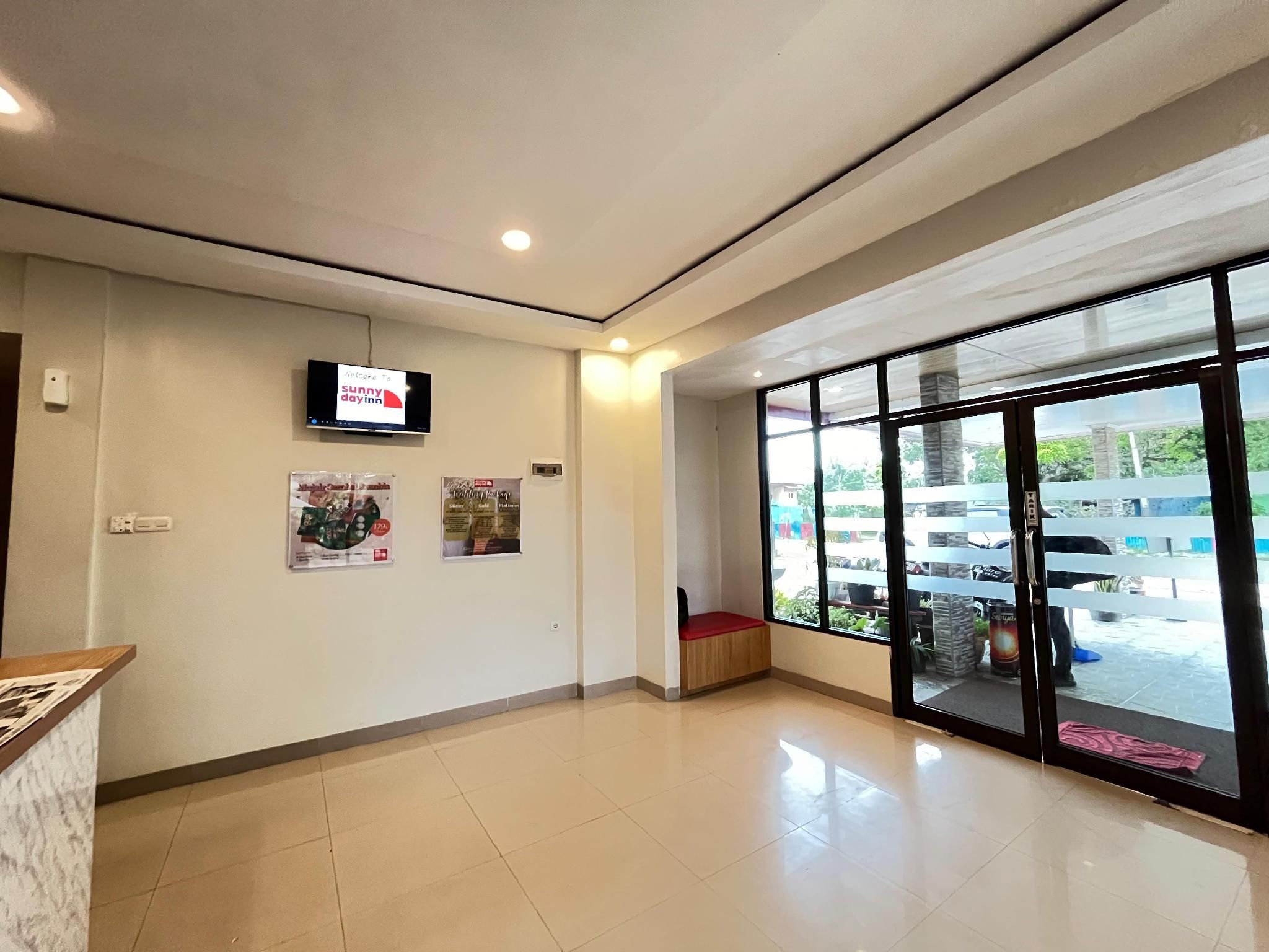 A clean, well-lit lobby with a reception desk, a television screen displaying a welcome message, and a large window offering a view of the parking area.
