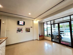 A clean, well-lit lobby with a reception desk, a television screen displaying a welcome message, and a large window offering a view of the parking area.