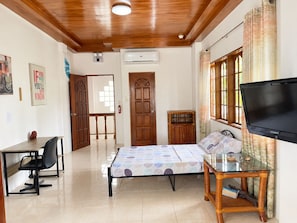 A room with a bed, a desk, a chair, a television, and a window with curtains.