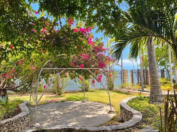 A garden with a stone pathway, a metal pergola, and pink flowering plants.