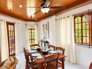 A dining area with a wooden table set for four, a ceiling fan, and a large window with curtains.