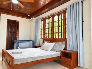 A bedroom with a wooden bed, a nightstand, a blue baby crib, and a window with curtains.