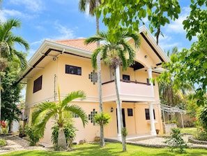 A two-story house with a balcony, surrounded by palm trees and a well-maintained garden.