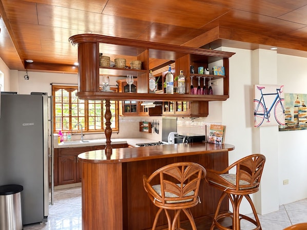 A kitchen with a wooden bar, two wicker chairs, and a refrigerator.