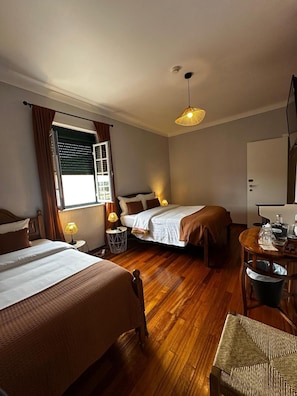 Una habitación de hotel con dos camas, piso de madera, una mesa de comedor y una lámpara colgante.