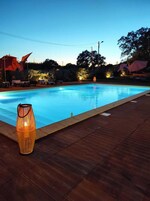 Una piscina con cubierta de madera, una lámpara decorativa y sillones de descanso al fondo.