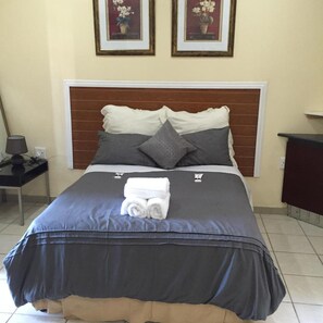 A neatly made bed with a dark blue bedspread, two pillows, and a folded towel on the bed. - Norwegian Lodge (Umkomaas)
