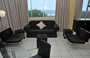 A modern living room with a black sofa, two black armchairs, a glass coffee table, and a view of the sea through large windows. - Norwegian Lodge (Umkomaas)