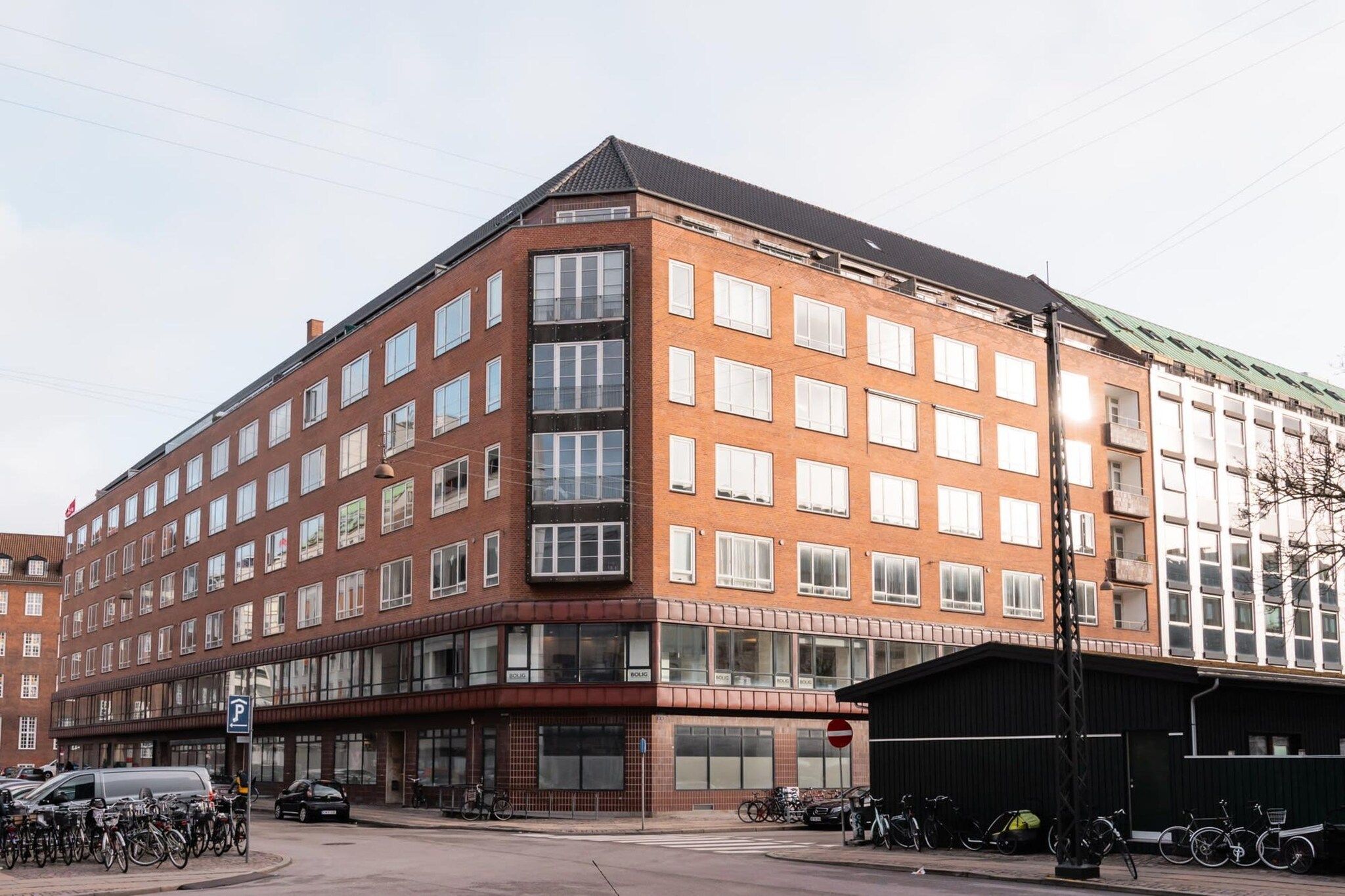 A multi-story building with a corner entrance, large windows, and a parking area with bicycles.