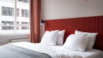 A hotel room with a bed, a window with curtains, and a view of buildings outside.