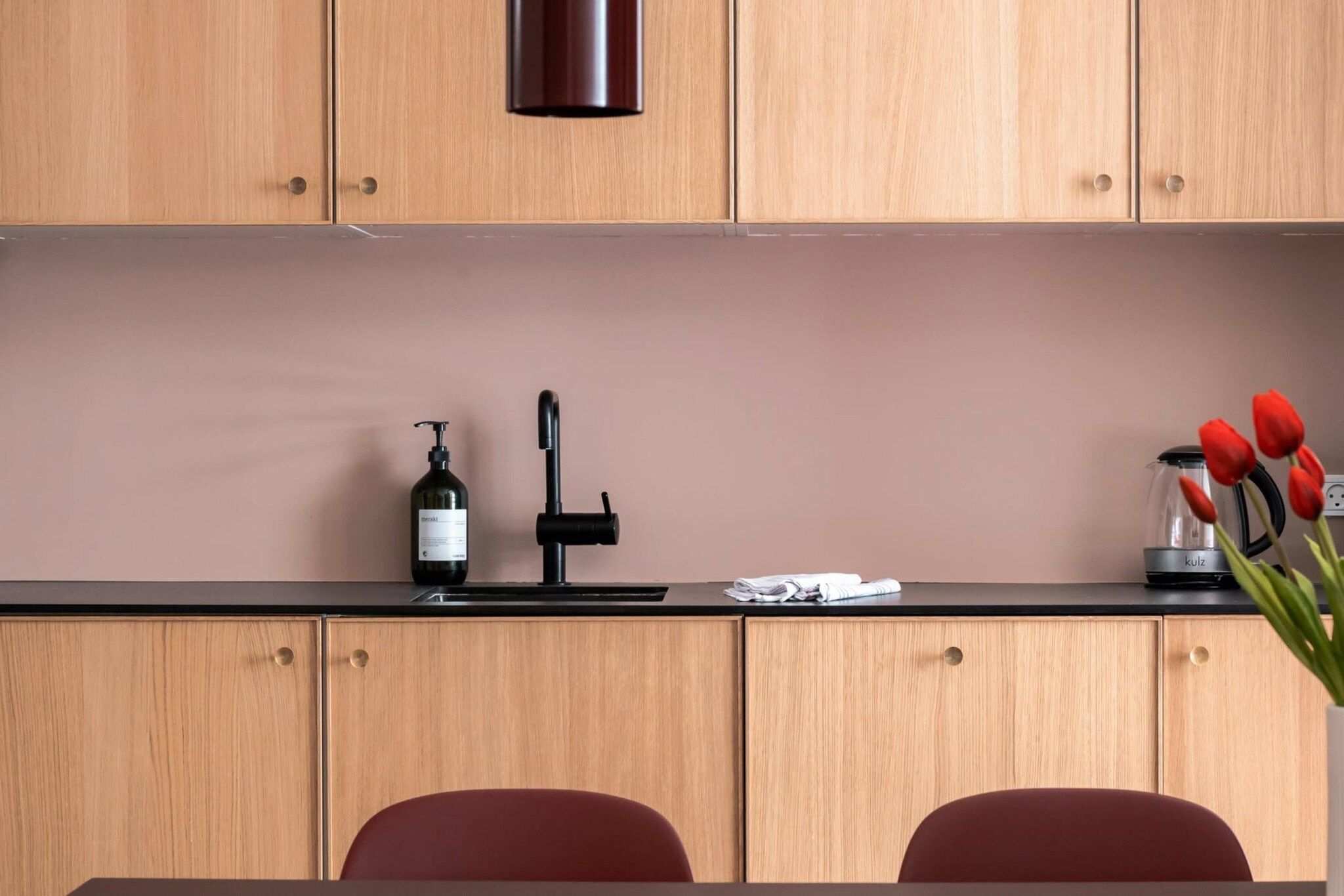 A kitchen with wooden cabinets, a black countertop, a bottle of shampoo, a hairdryer, and red tulips.
