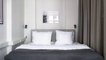 Een hotelkamer met een bed, twee bedlampen, een raam met gordijnen en een foto in een lijst aan de muur.