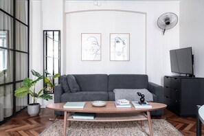 Een woonkamer met een grijze bank, een bijzettafeltje, een plant en twee ingelijste kunstwerken aan de muur.