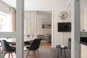 Een moderne woonkamer met een eethoek, een flatscreen televisie aan de muur en een groot raam met gordijnen.