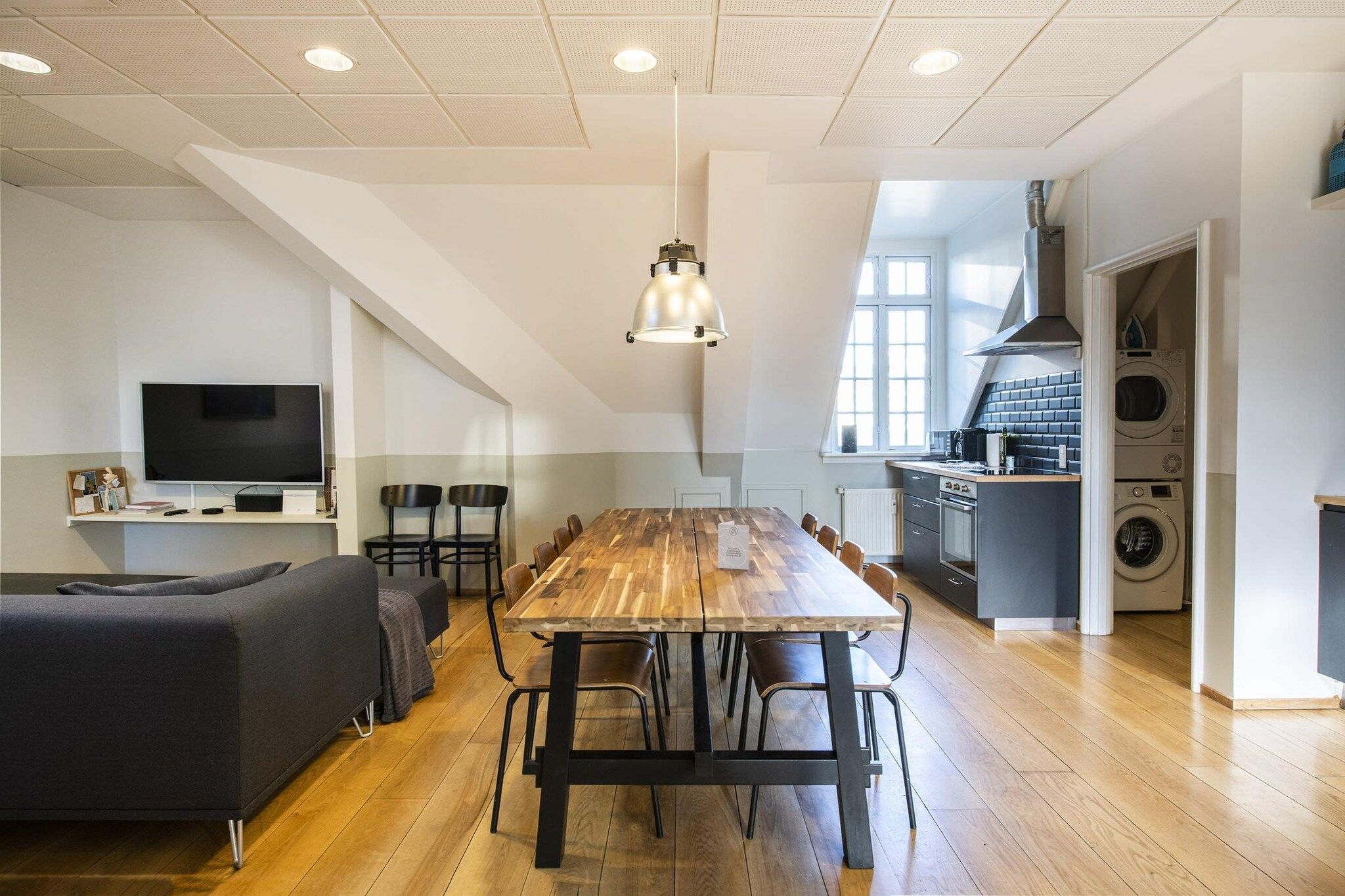 Et moderne køkken med en stor ø, et spiseområde med et træbord og stole, samt en opholdsstue med sofa og lænestole.