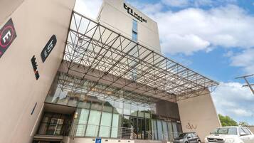 Um hotel moderno com fachada de vidro, cobertura em estrutura metálica e uma placa indicando ser um 'TRI Hotel Executive'.