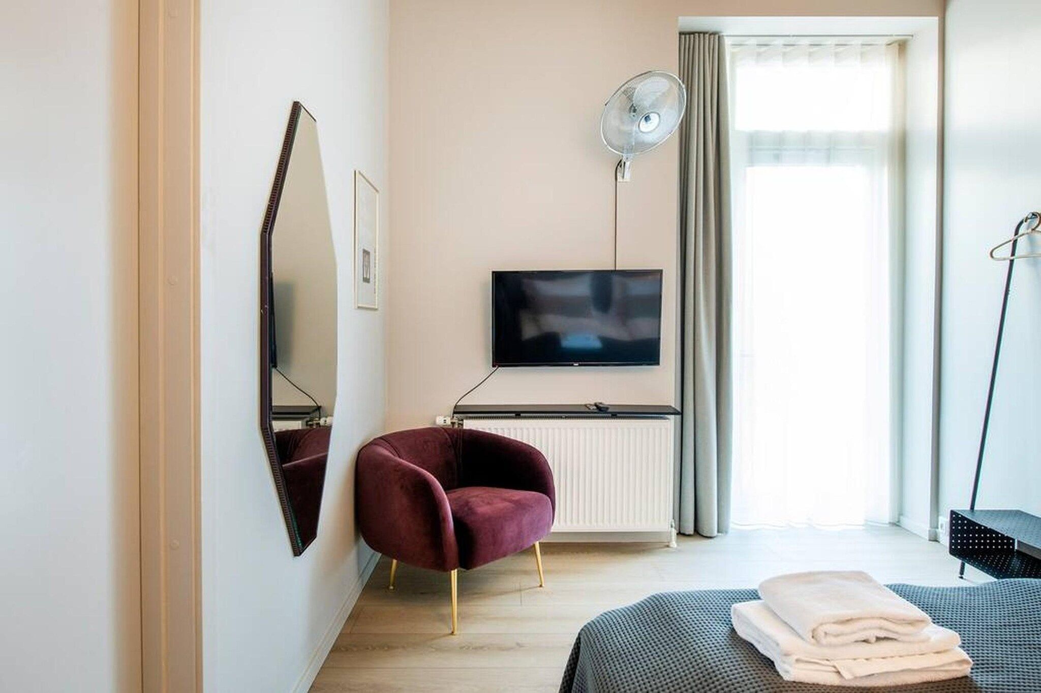 Ein Hotelzimmer mit Bett, Fernseher, Stuhl, Heizkörper und einem Fenster mit Vorhängen.