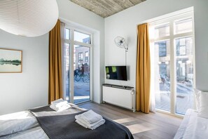 A hotel room with a bed, a flat-screen TV, a radiator, and large windows with curtains. - Spacious Stay with Gym (København)
