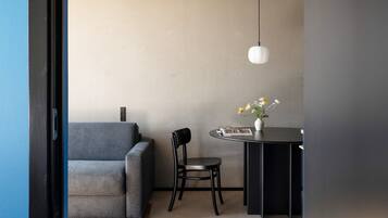 A room with a grey sofa, a black chair, a small round table with a vase of flowers, and a hanging light fixture.