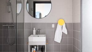 A modern bathroom with a shower, a sink with toiletries, and a mirror. - Aarhus Stay with Free Parking (Aarhus)