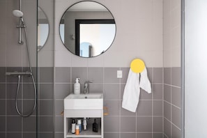 Un baño moderno con ducha, lavamanos y artículos de aseo, y un espejo.